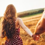 Rear view of a woman with long red hair holding her boyfriend's hand